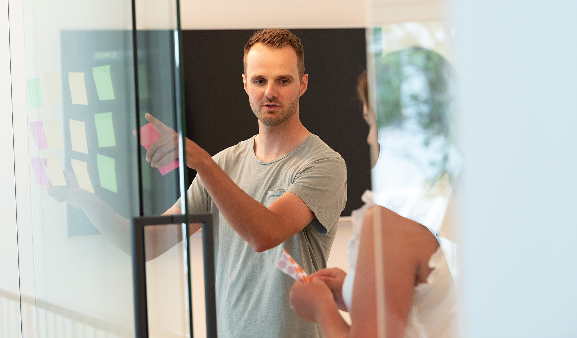 Ideenfindung 2 Menschen stehen in einem modernen Konferenzraum und hängen Klebezettel an eine Glaswand