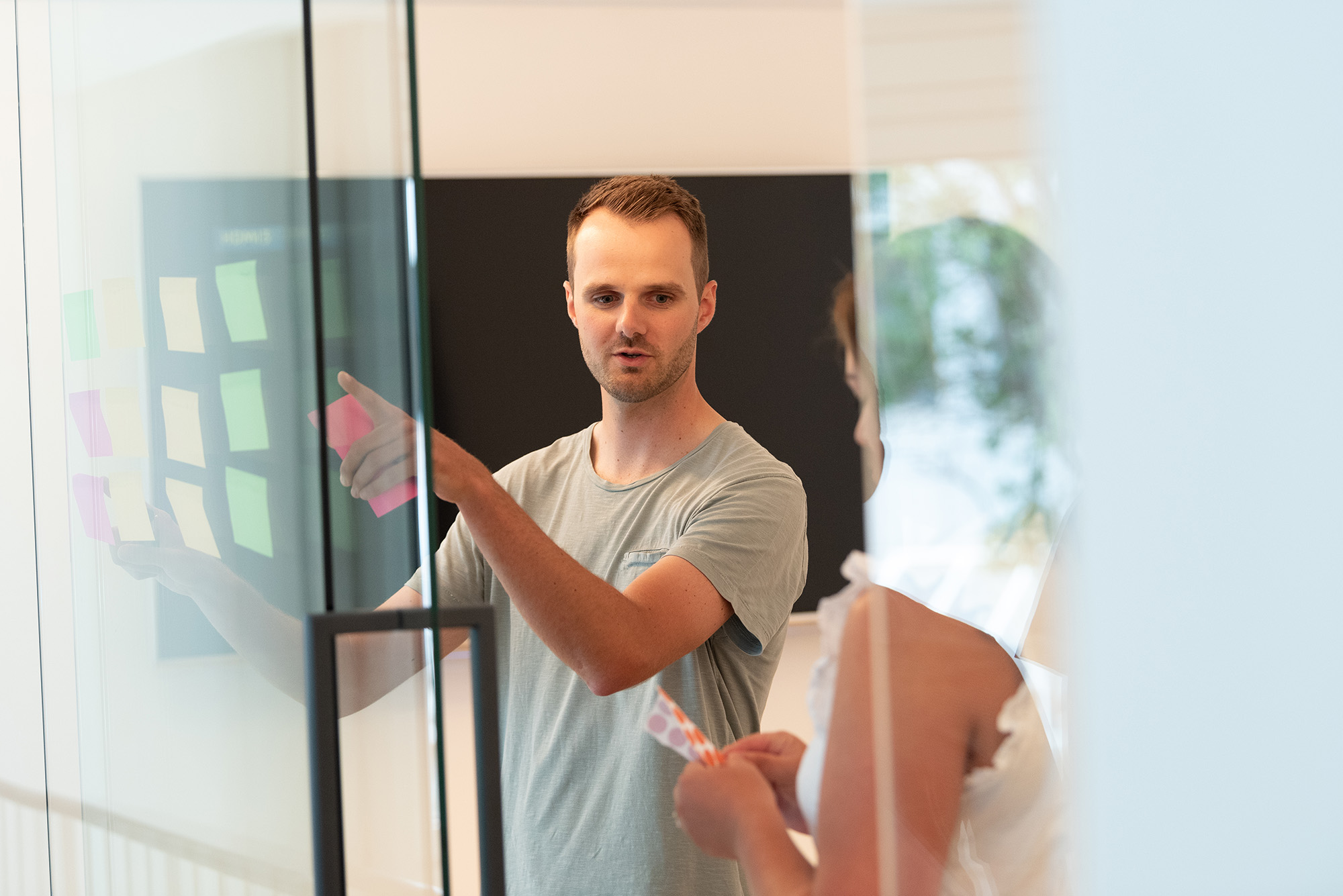 Ideenfindung 2 Menschen stehen in einem modernen Konferenzraum und hängen Klebezettel an eine Glaswand